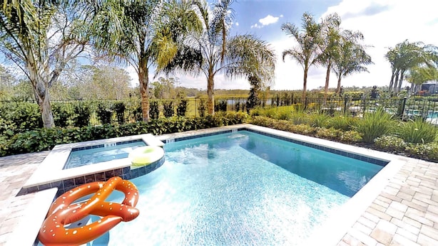 A swimming pool with a hot tub, surrounded by lush greenery and palm trees. - Encore Resort at Reunion 7511 (Kissimmee)