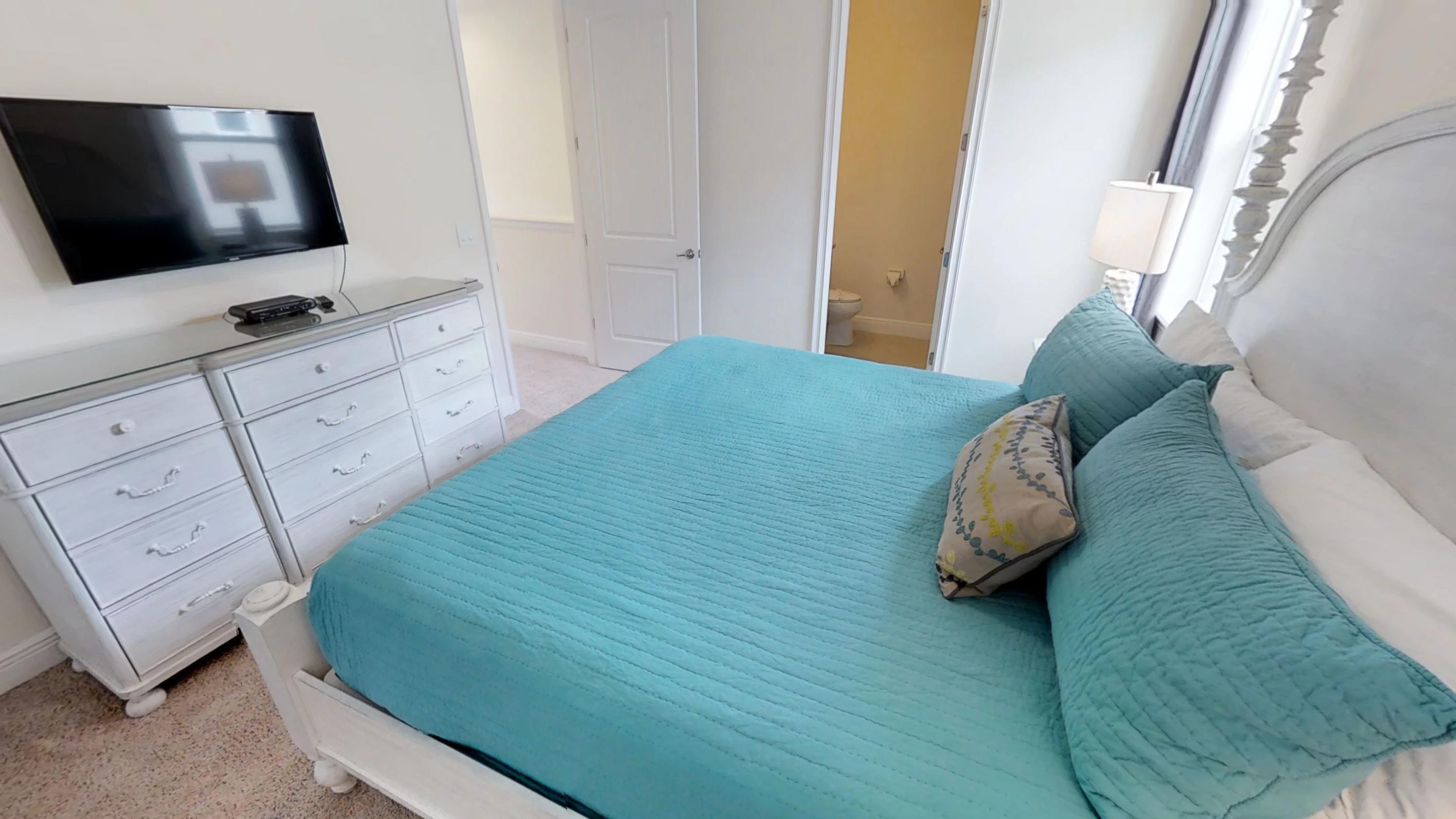 Un dormitorio con cama, televisor, cómoda y puerta.