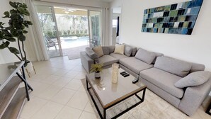 A modern living room with a grey sectional sofa, a glass coffee table, and a large abstract painting on the wall. - Encore Resort at Reunion 7511 (Kissimmee)
