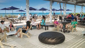 Ett utomhusområde med sittplatser, bord och stolar, parasoller och utsikt över stranden.