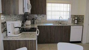 Una cocina moderna con armarios de madera oscura, encimera de granito, lavavajillas integrado y una ventana con persianas.