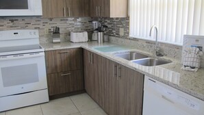 Una cocina con armarios de madera, microondas, tostadora, lavaplatos y un fregadero.