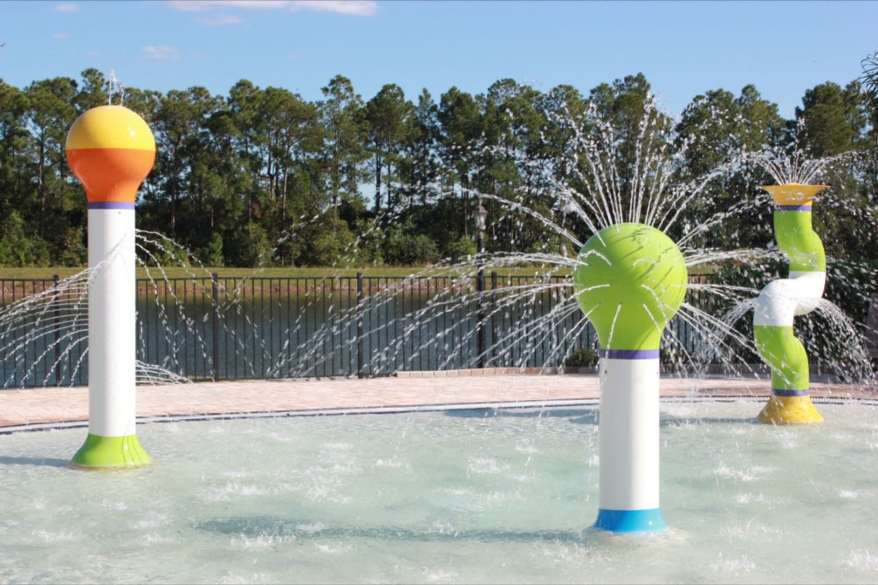Een waterattractie met meerdere fonteinen, omringd door een hek en bomen op de achtergrond.