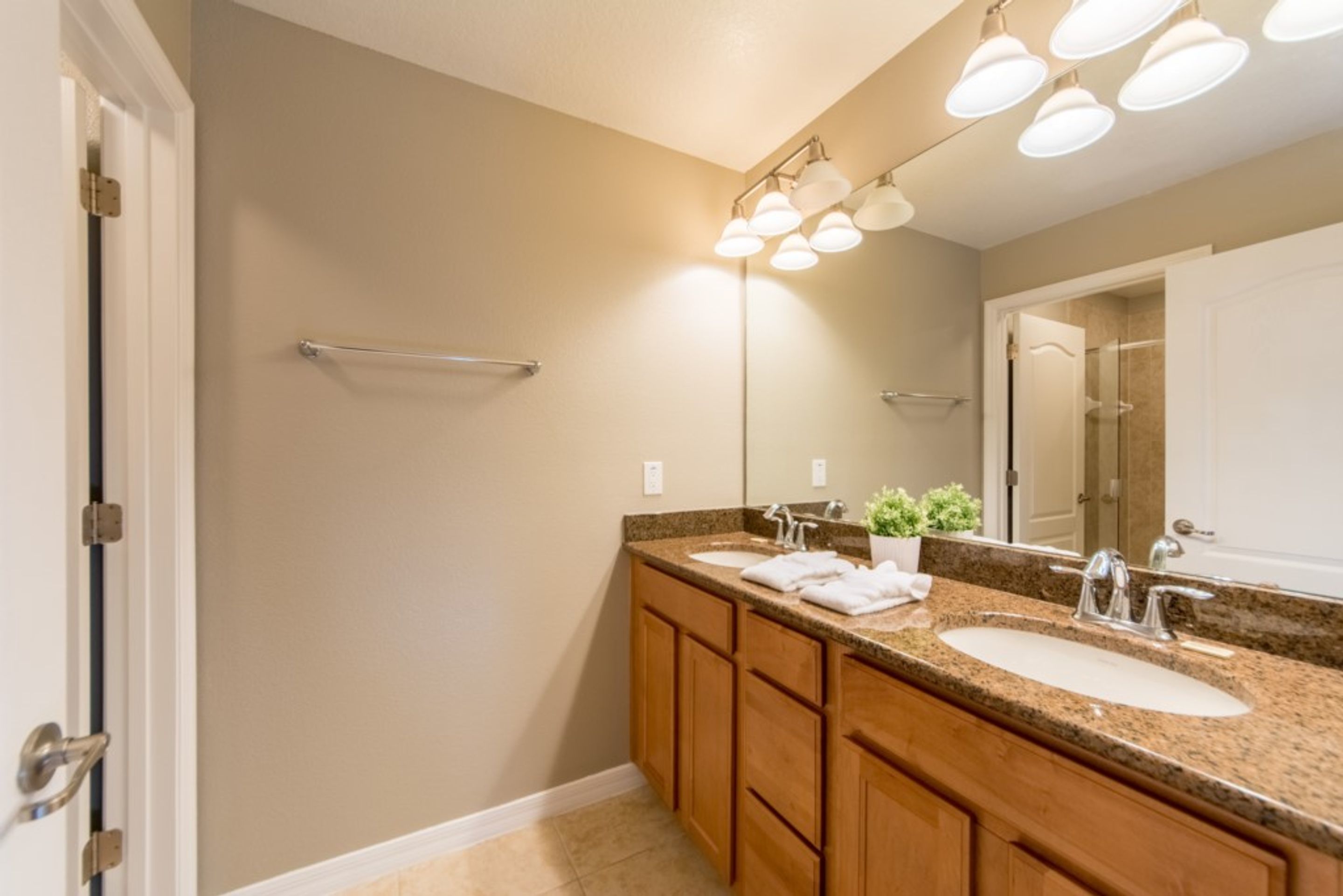 A bathroom with two sinks, wooden cabinets, a towel rack, and a mirror with lights above.