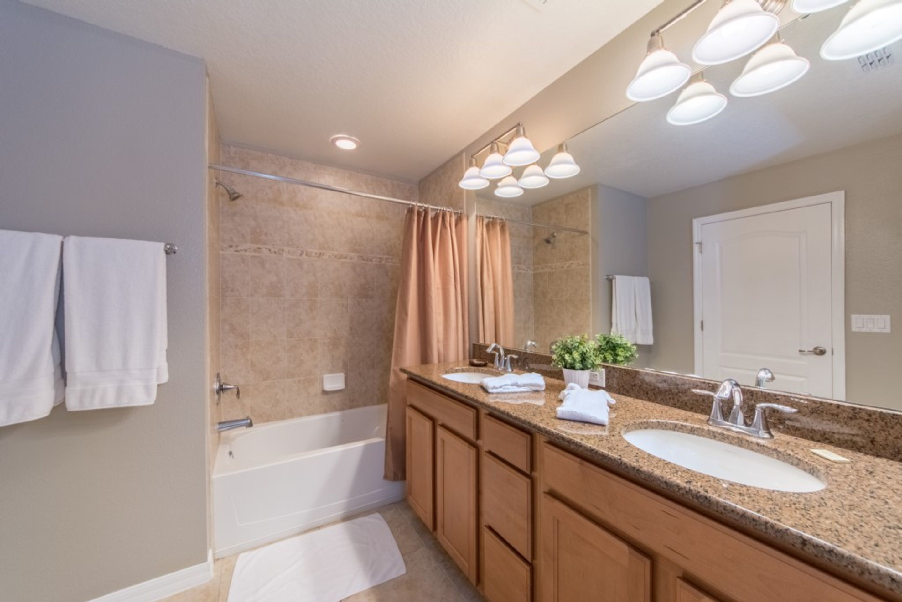 A modern bathroom with a bathtub, double sink vanity, and a large mirror.
