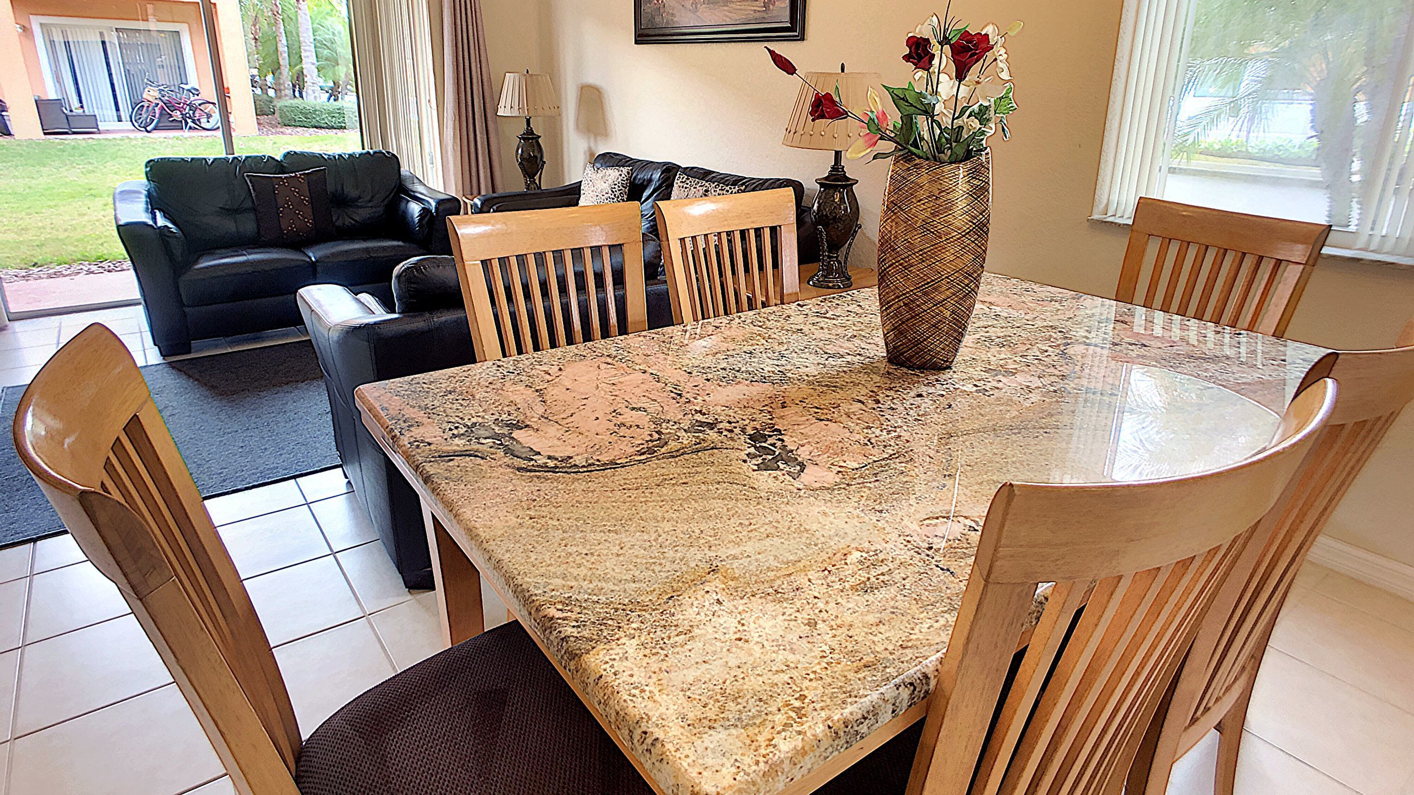 A dining area with a marble table, wooden chairs, and a vase with flowers.