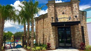 A fitness center with a brick facade, a black entrance, and palm trees in the foreground. - Festival Resort 342 (Davenport)