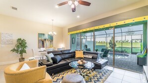 A modern living room with a black leather sofa, a glass coffee table, and a yellow armchair. There is a large window with a view of a garden. - Festival Resort 342 (Davenport)