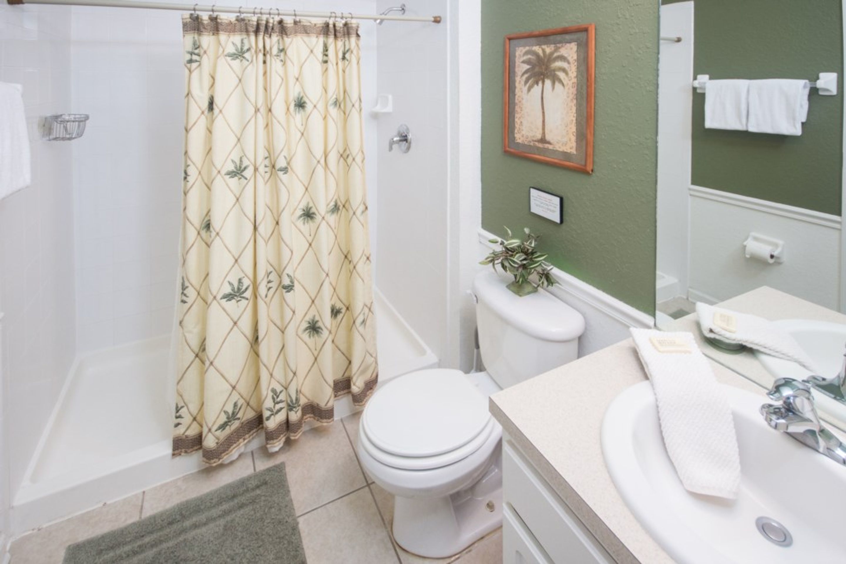 A bathroom with a shower, toilet, sink, and a framed picture on the wall.
