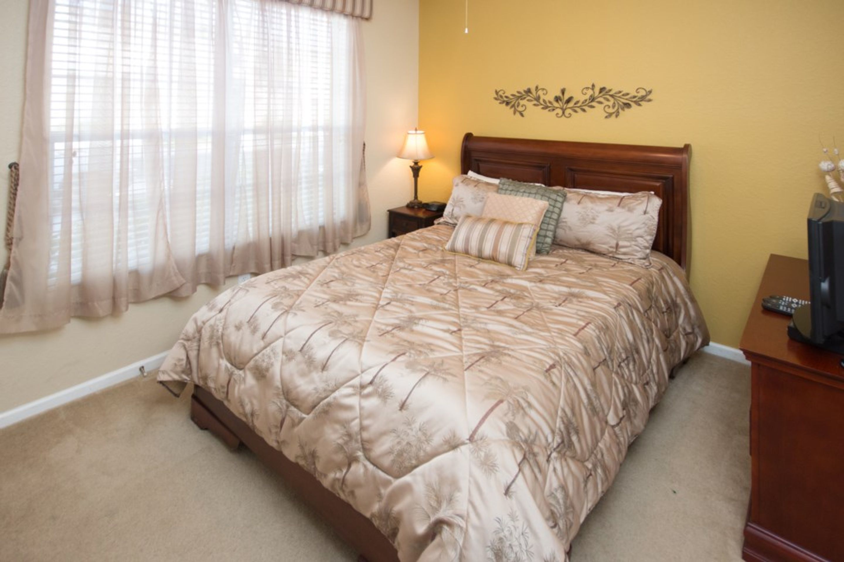 A bedroom with a large bed, a nightstand with a lamp, and a decorative wall piece.