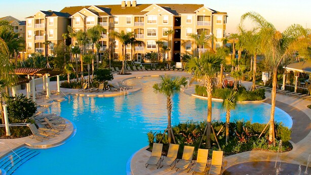 Ein Resort mit zentralem Schwimmbad, Palmen und einem mehrstöckigen Gebäude mit Balkonen.