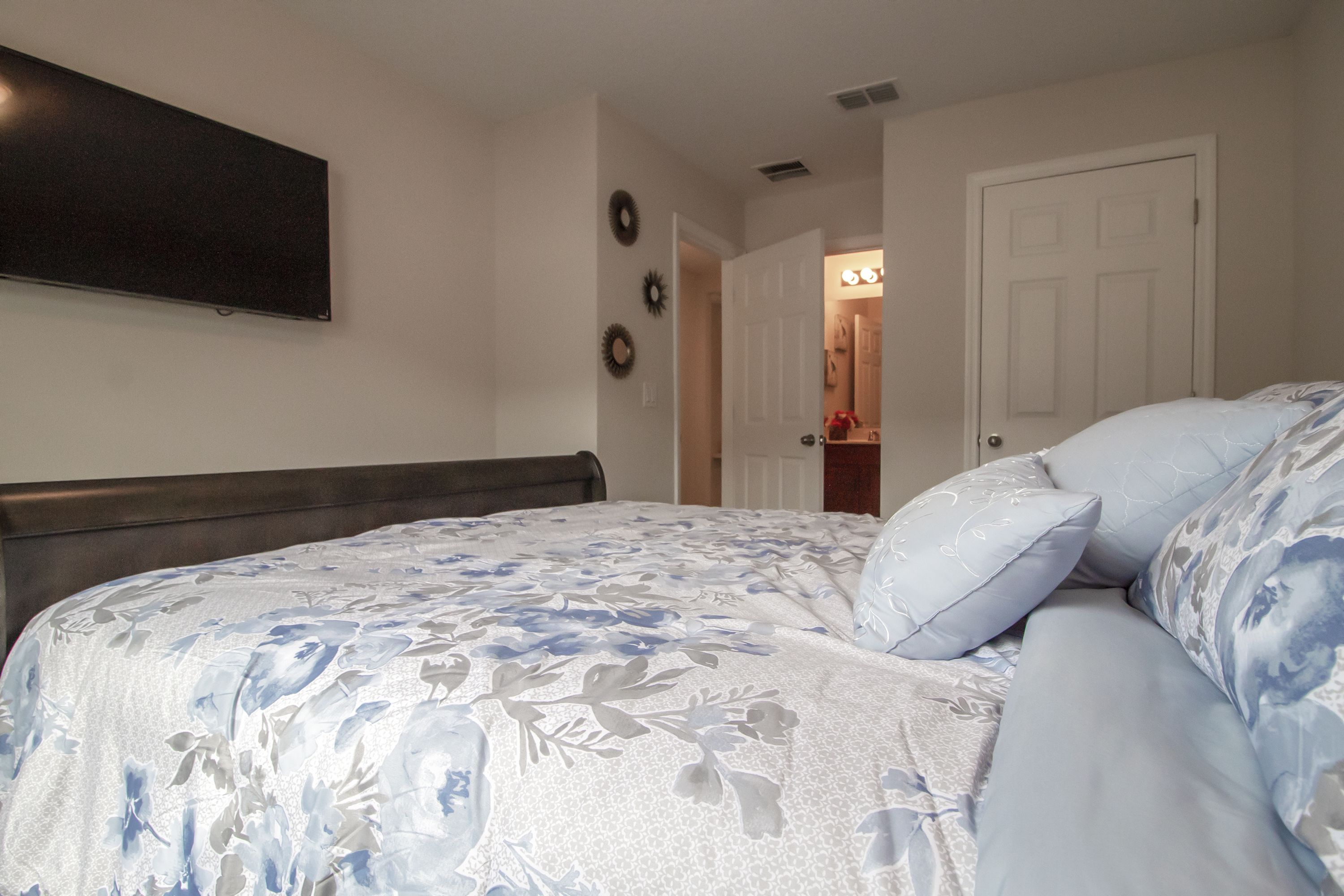 A bedroom with a bed, a wall-mounted TV, and a door leading to a bathroom.