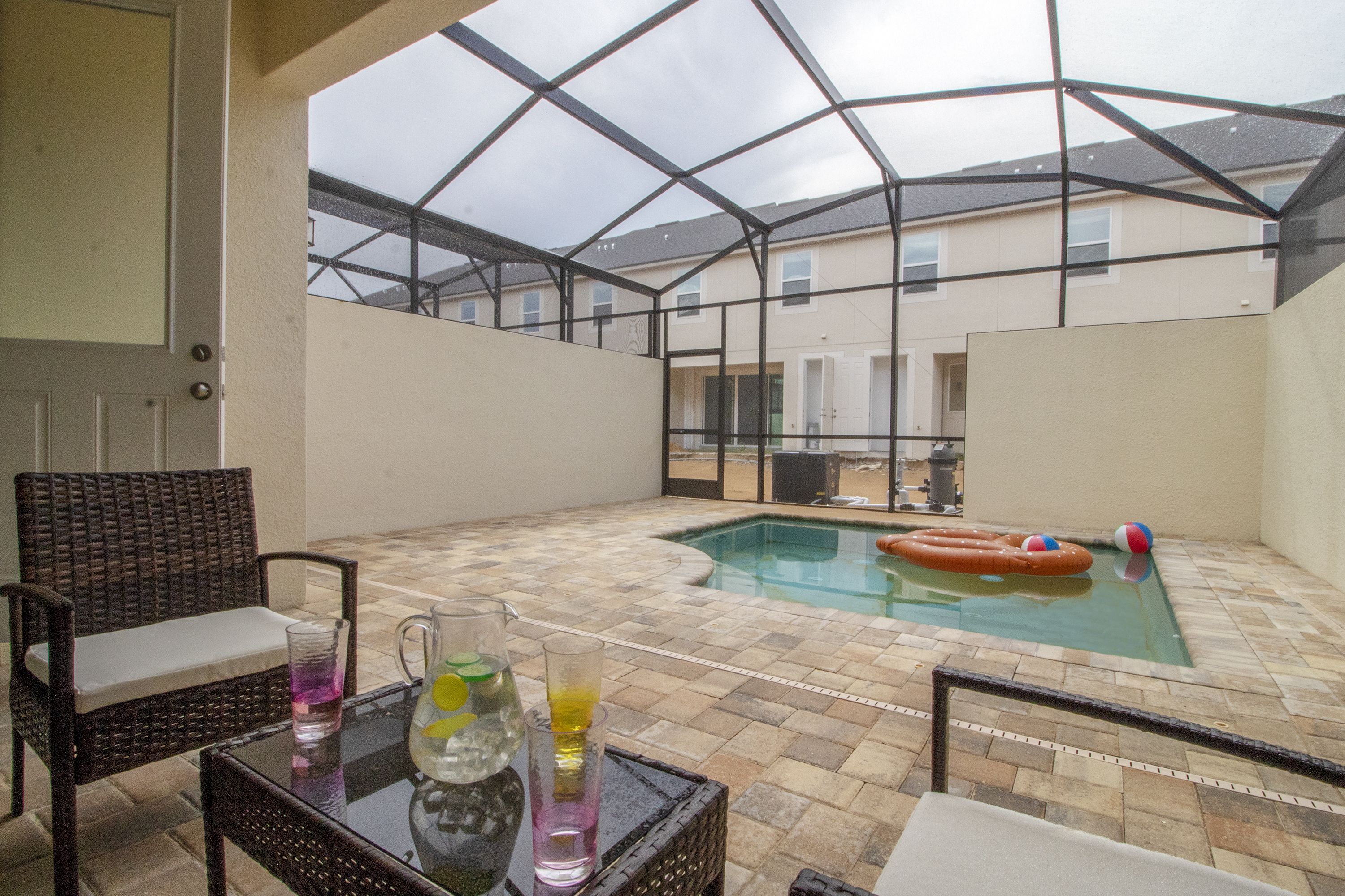 An outdoor patio with a pool, wicker furniture, and a glass table with drinks.