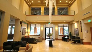 Een ruime lobby met een hoge plafond, een kroonluchter, comfortabele zitplaatsen, een receptiebalie en grote ramen.