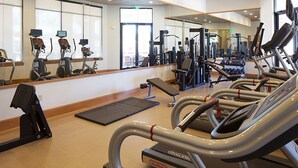 Een fitnessruimte met loopbanden, krachtapparaten en een spiegelwand.