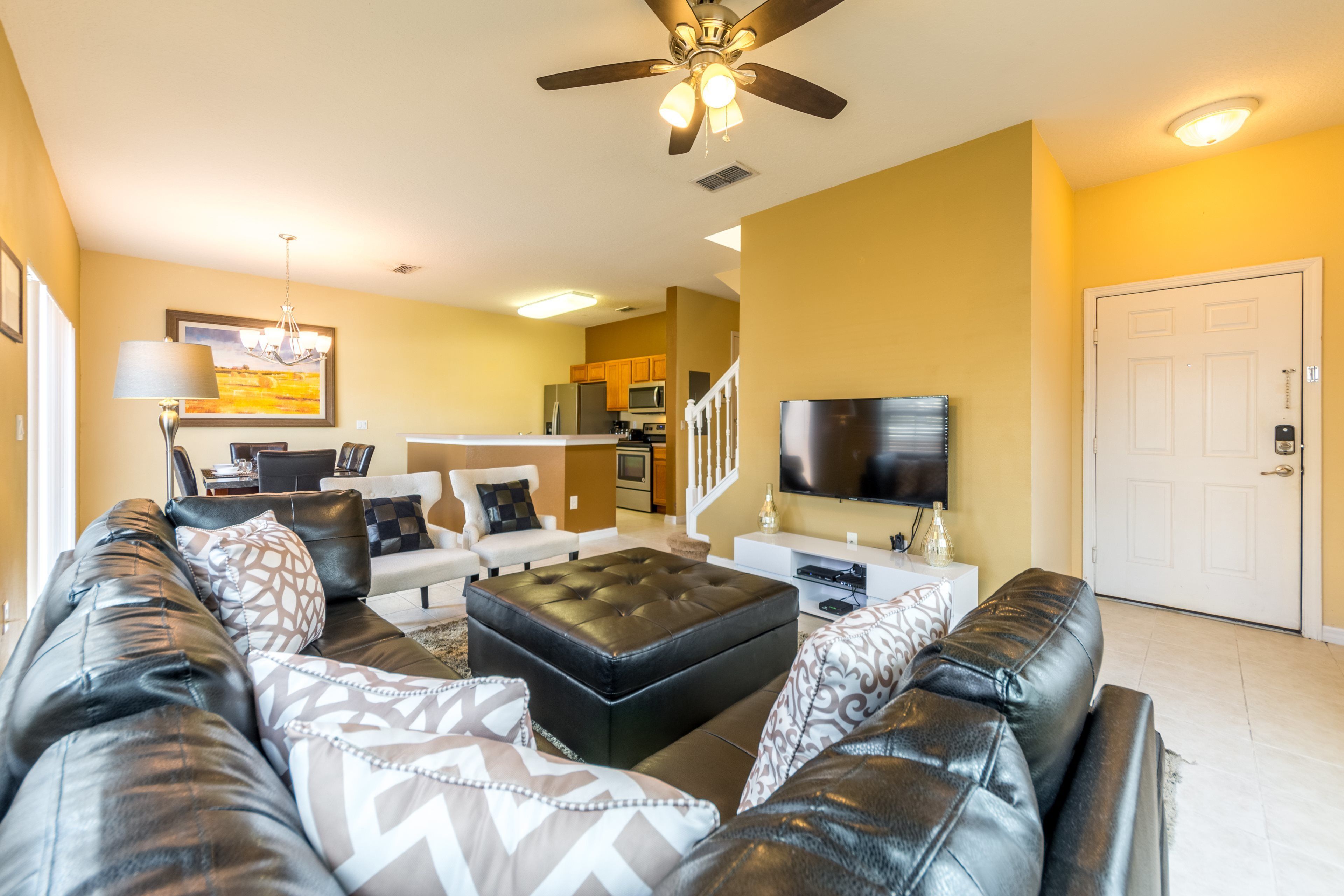 A living room with a black leather sofa, a black ottoman, and a flat-screen TV.