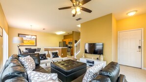 A living room with a black leather sofa, a black ottoman, and a flat-screen TV. - Bella Vida 4561 (Kissimmee)