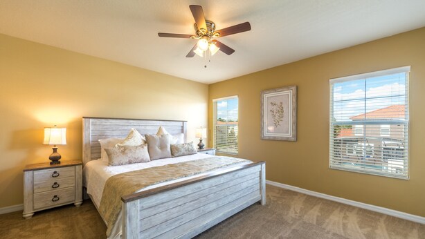 A bedroom with a wooden bed, nightstands, a ceiling fan, and a window with blinds. - Bella Vida 4561 (Kissimmee)