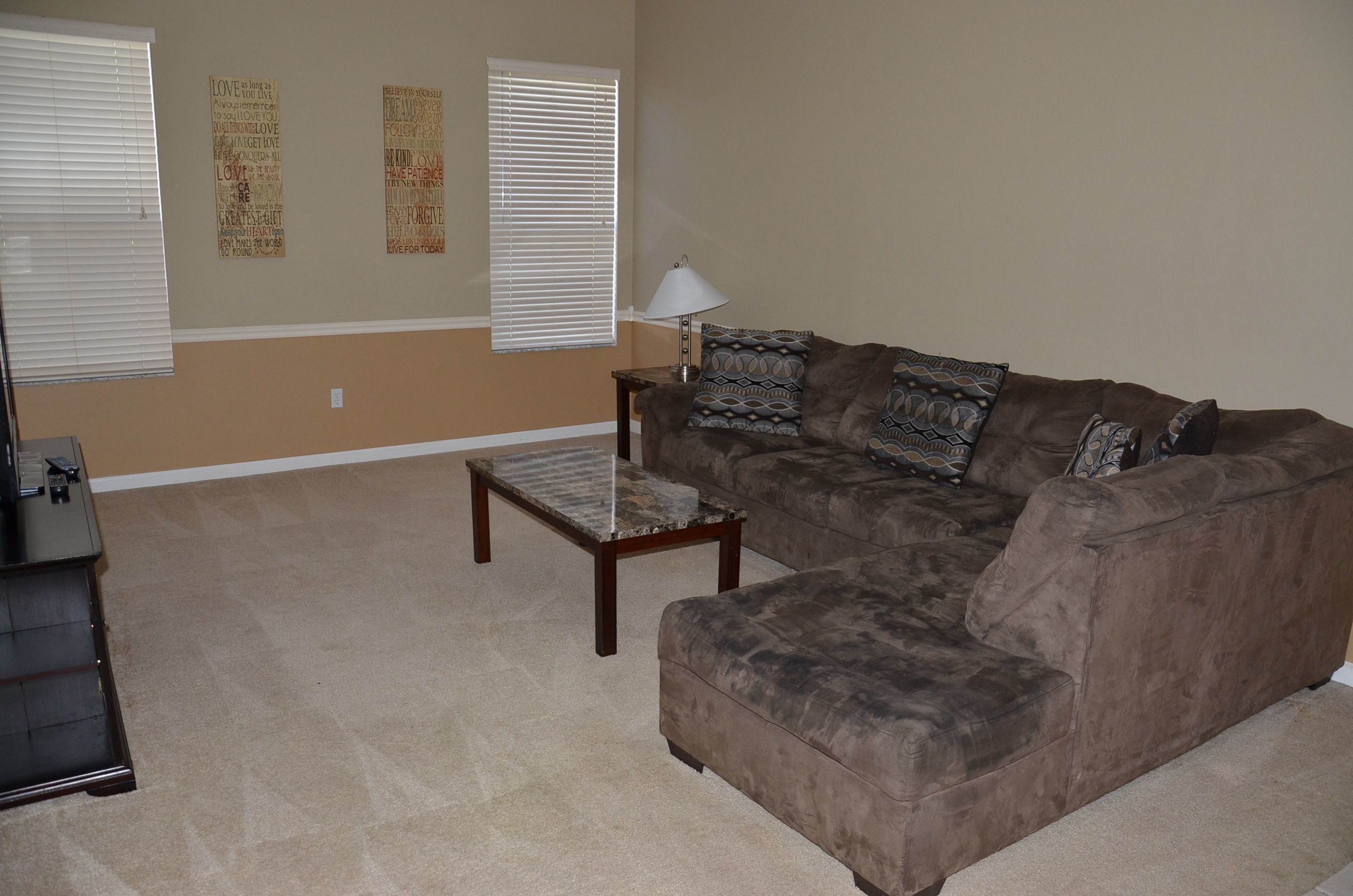 A living room with a brown couch, a small wooden coffee table, and two windows with blinds.