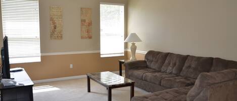A living room with a brown couch, a coffee table, a lamp, and a TV on a stand.