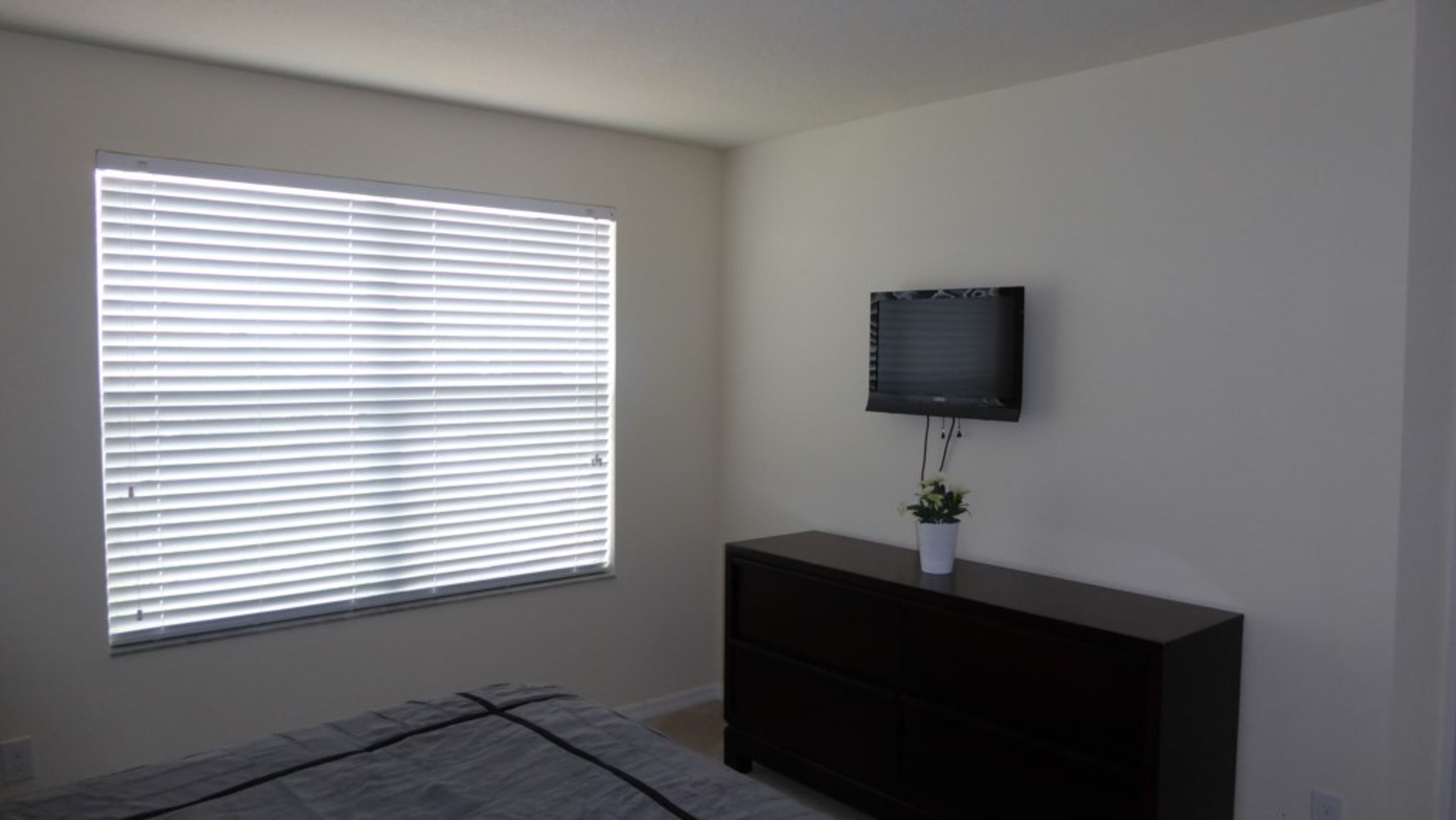 Een slaapkamer met een groot raam, een wandtelevisie en een donkere dressoir.
