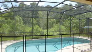 Une piscine couverte dotée d’une structure métallique et de panneaux de verre, entourée d’une clôture de sécurité.