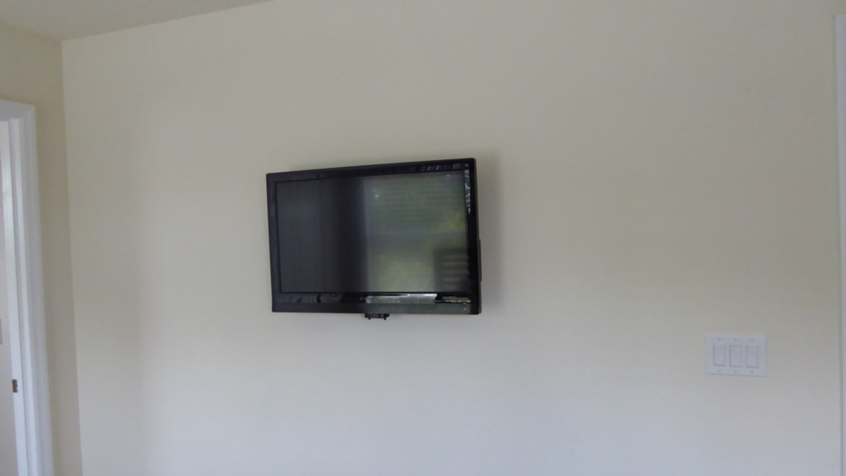 A television mounted on a plain wall in a room with a door on the left.