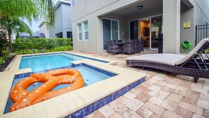 A swimming pool with a polka-dotted inflatable ring, a lounge chair, and a patio area with a table and chairs. - Encore Resort at Reunion 410 (Kissimmee)