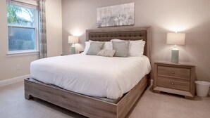 A bedroom with a large bed, two bedside tables, a nightstand, and a window with curtains. - Encore Resort at Reunion 410 (Kissimmee)