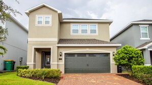 A two-story house with a garage, a small porch, and a well-maintained front yard with shrubs and a tree. - Encore Resort at Reunion 410 (Kissimmee)