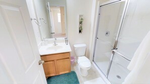 A bathroom with a white sink, wooden vanity, toilet, and a glass shower enclosure. - Bella Vida 540 (Kissimmee)