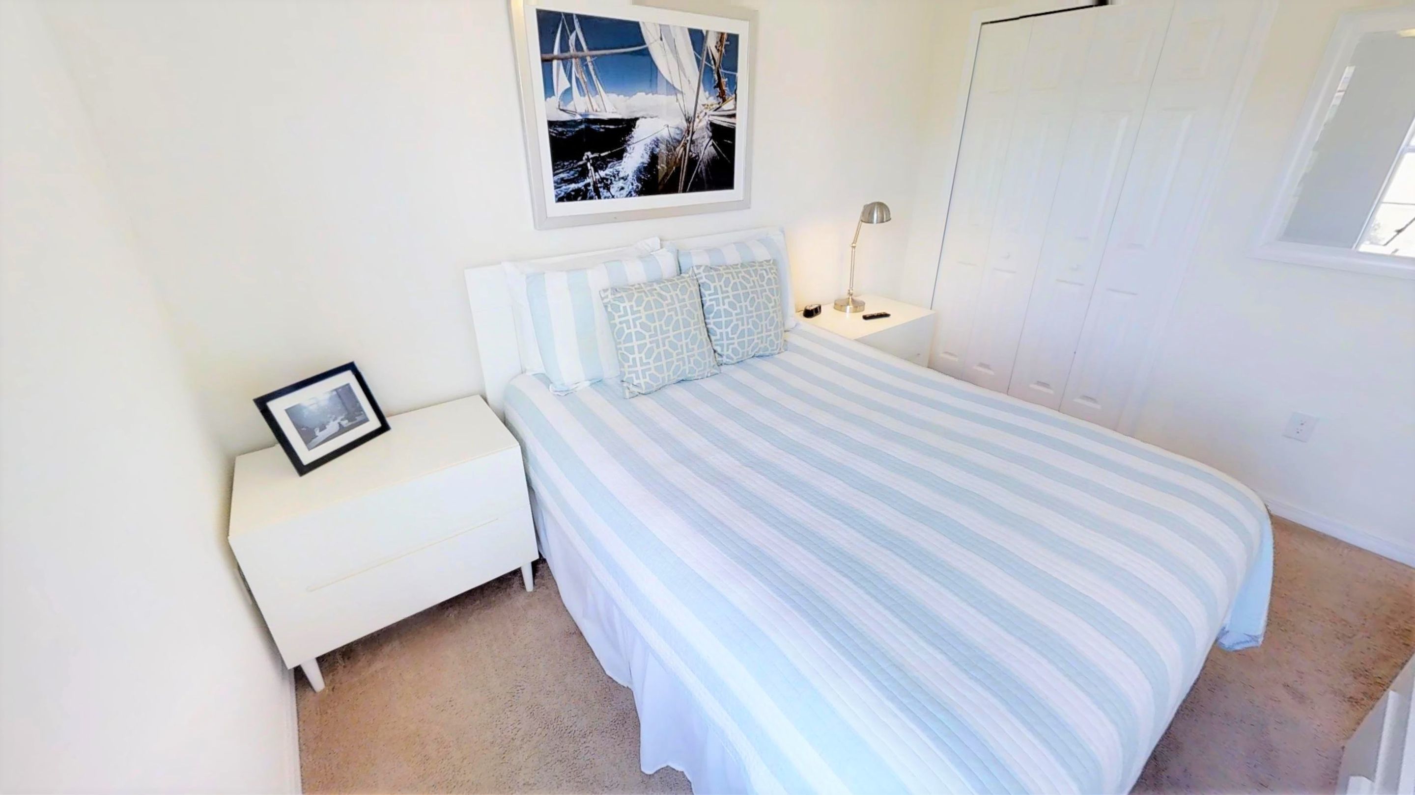 A bedroom with a bed, a nightstand, a framed picture, a lamp, and a wardrobe.
