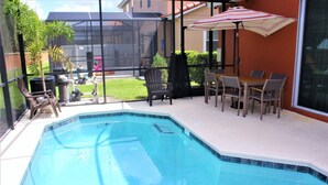 Una piscina con area solarium, inclusi sedie e un tavolo, e vista su un quartiere residenziale.