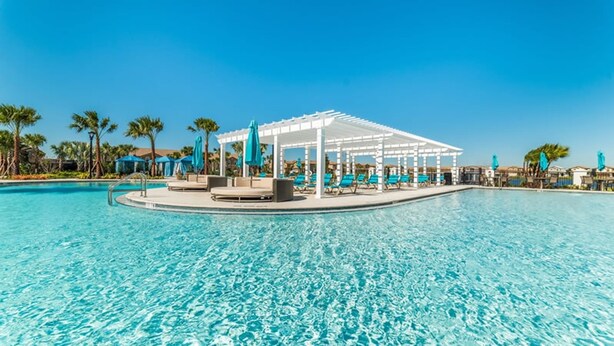 Piscina cristallina blu con un pergolato bianco e poltrone da relax.