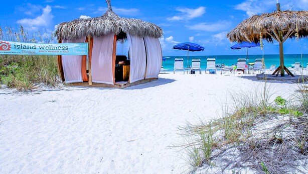 Ett wellnesscenter vid stranden med en byggnad med halmtak, strandstolar och parasoller.
