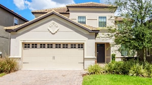 Une maison à deux étages avec une porte de garage de couleur beige, un petit porche à l’avant et un toit recouvert de tuiles.