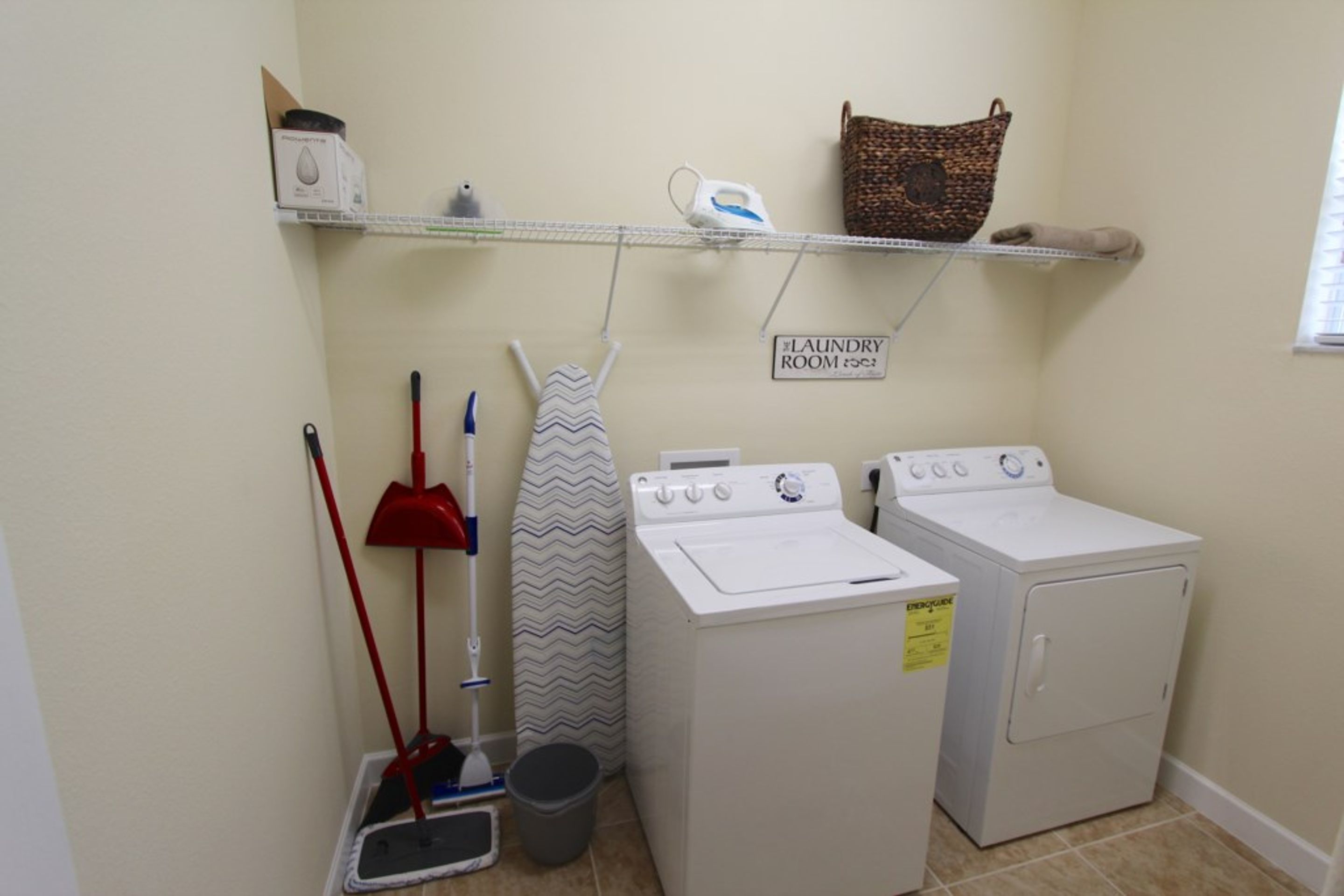 A laundry room with a washing machine, dryer, iron, and mops.