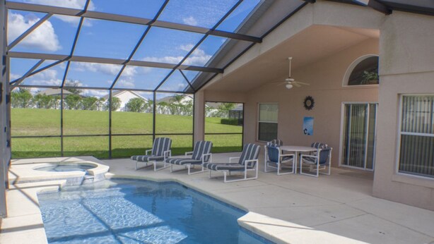 A covered swimming pool with lounge chairs and a hot tub, surrounded by a patio area.