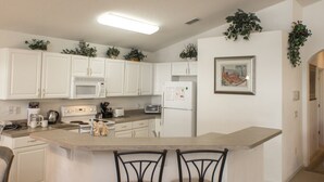 A modern kitchen with white cabinets, a central island with bar stools, a microwave, a refrigerator, and a toaster.
