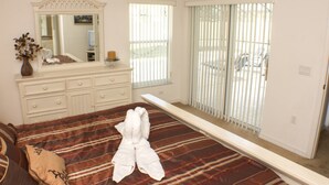 A bedroom with a large bed, a dresser, a mirror, and a window with blinds.