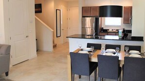 A modern kitchen with a central island, dining area with chairs, and a staircase leading to another level. - Regal Oaks 2714 (Kissimmee)