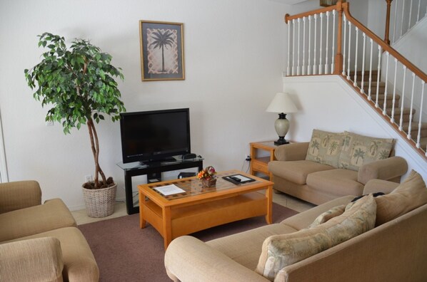 A living room with a television, a coffee table, a sofa, a lamp, and a staircase.
