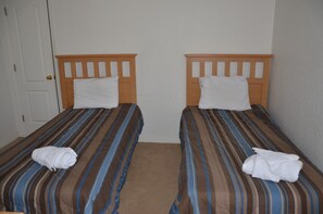 Two single beds with striped bedding and wooden headboards in a room with white walls and a door.