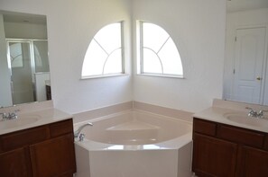 A bathroom with two sinks, a large bathtub, and arched windows.