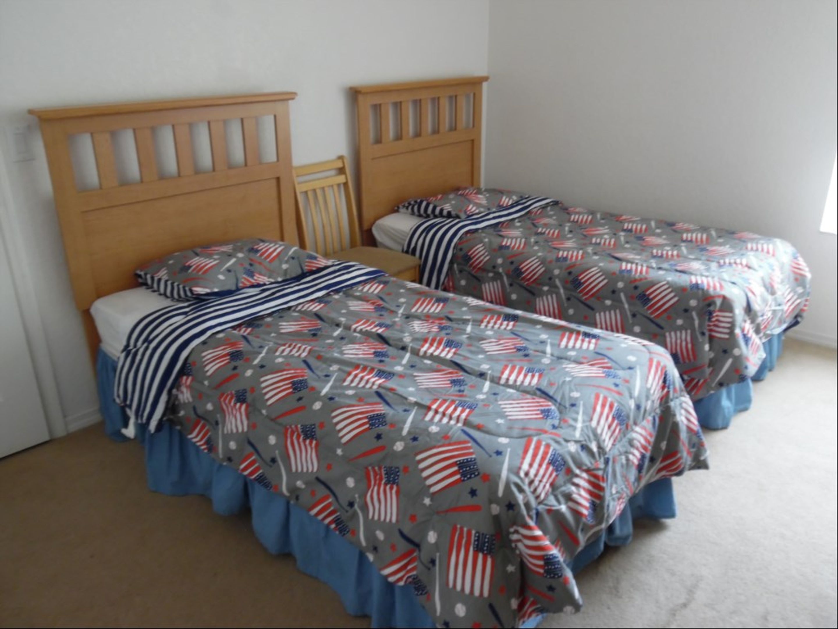 Un dormitorio con dos camas individuales, cada una con cabecero de madera y colcha gris con estampado de estrellas y rayas.