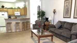 A living room with a grey sofa, a glass coffee table, and a kitchen area with wooden cabinets and a microwave. - Calabay Parc 410 (Davenport)