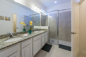 A modern bathroom with a granite countertop, a large mirror, and a glass shower enclosure.