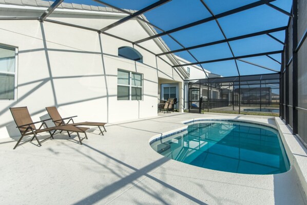 An indoor swimming pool with a glass enclosure, sun loungers, and a clear view of the sky.