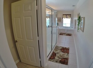 A hallway with a white door, a glass shower door, and a tiled floor.