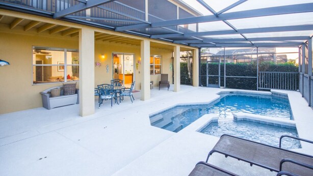 A covered outdoor swimming pool area with lounge chairs and a patio table. - The Shire at West Haven 1012 (Davenport)